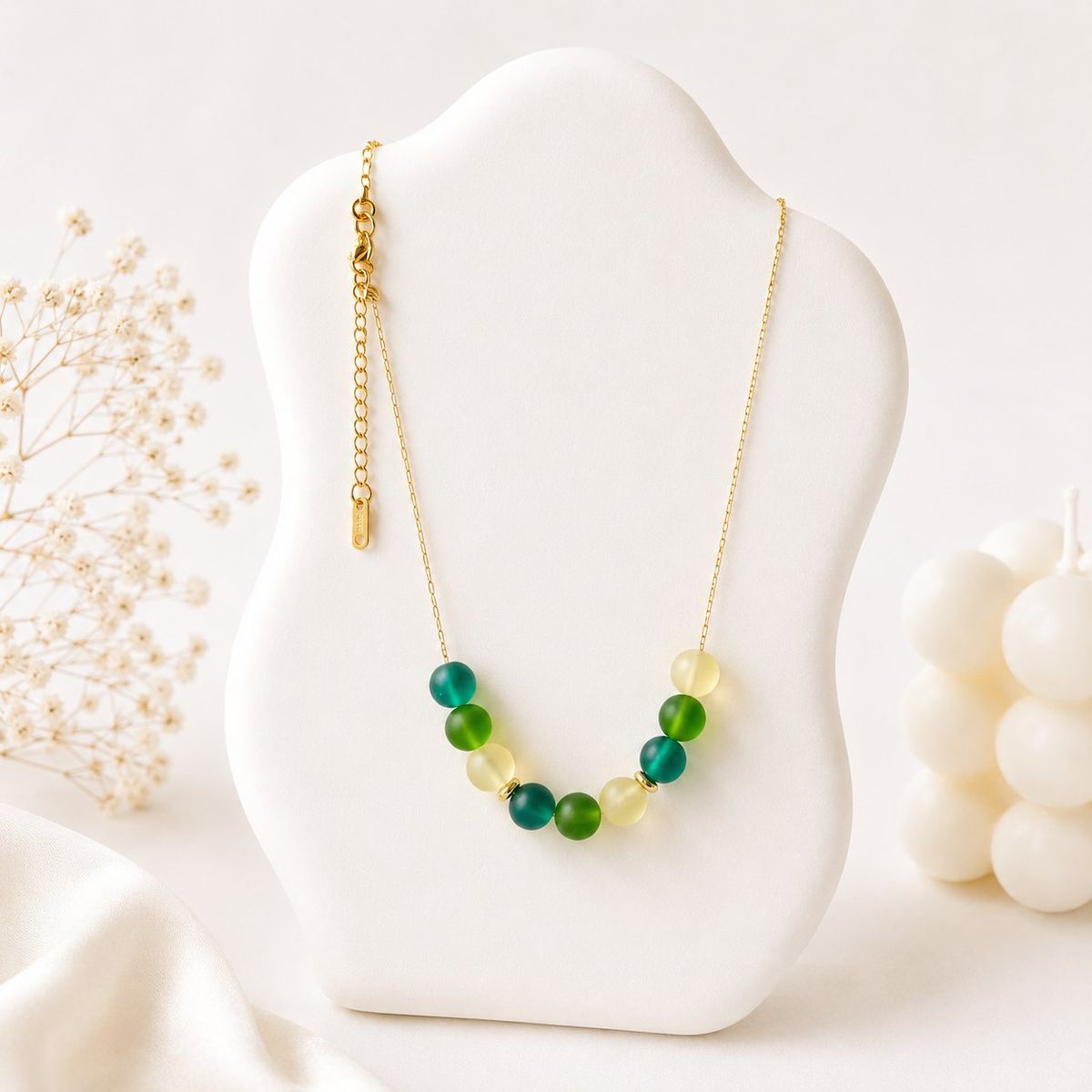 A gold chain necklace with a curved row of round green and yellow-green beads in frosted and glossy finishes displayed on a white jewelry bust.