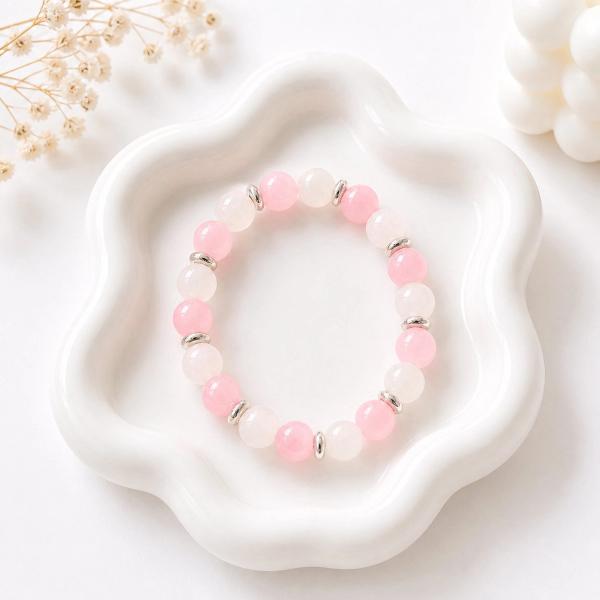 A stretch bracelet with alternating pink and white round beads and silver disc spacers, displayed on a white flower-shaped ceramic dish.