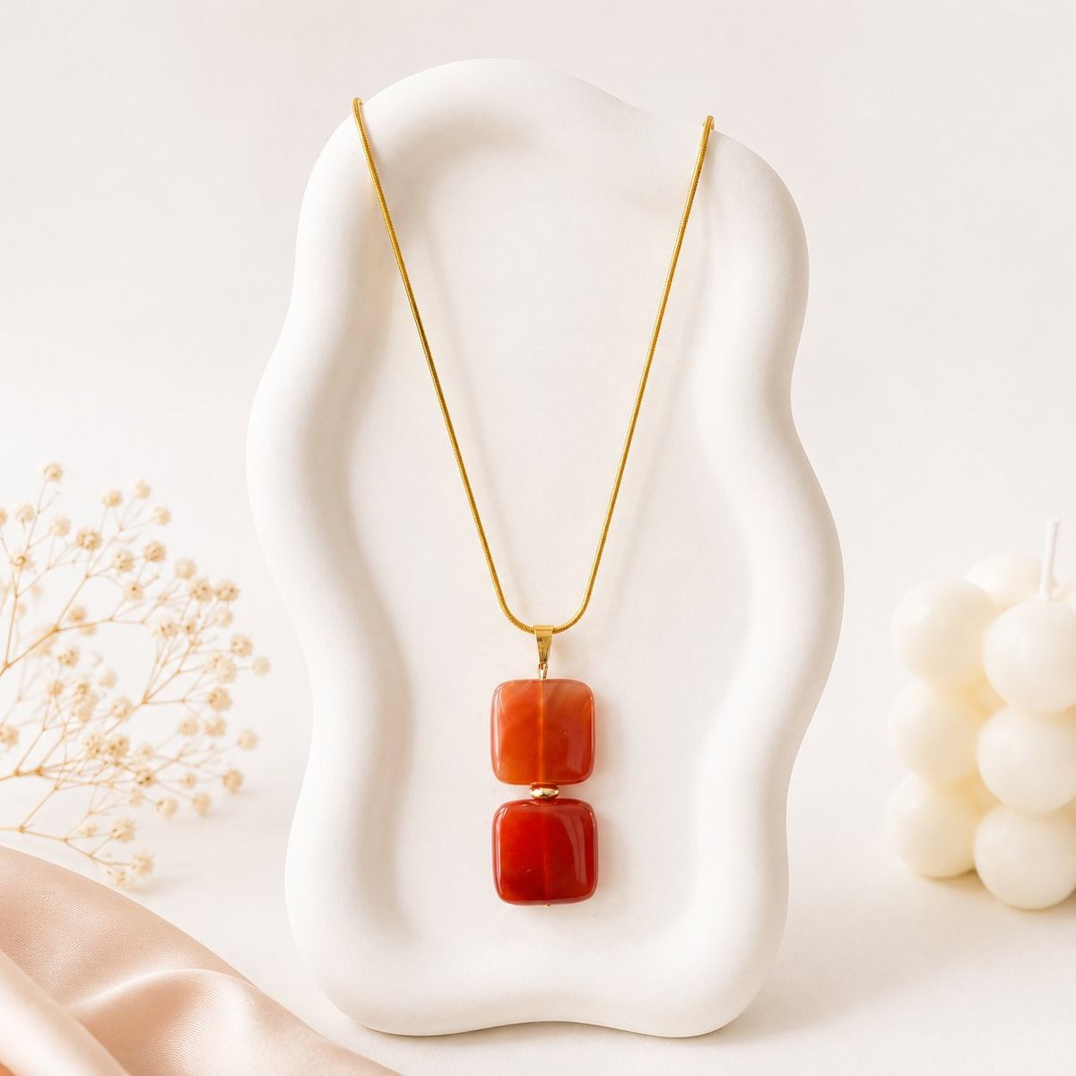 Gold snake chain necklace with two stacked rounded square red stone pendants displayed on a white sculptural jewelry bust.