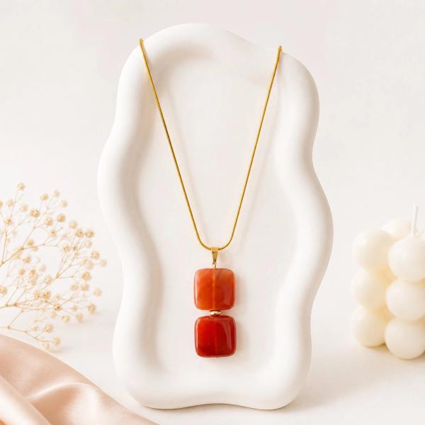 Gold snake chain necklace with two stacked rounded square red stone pendants displayed on a white sculptural jewelry bust.