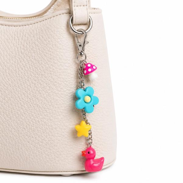 A silver-tone lobster clasp bag charm with four colorful resin charms — a pink rubber duck, yellow star, teal flower, and pink polka-dot mushroom — clipped to a cream leather handbag.