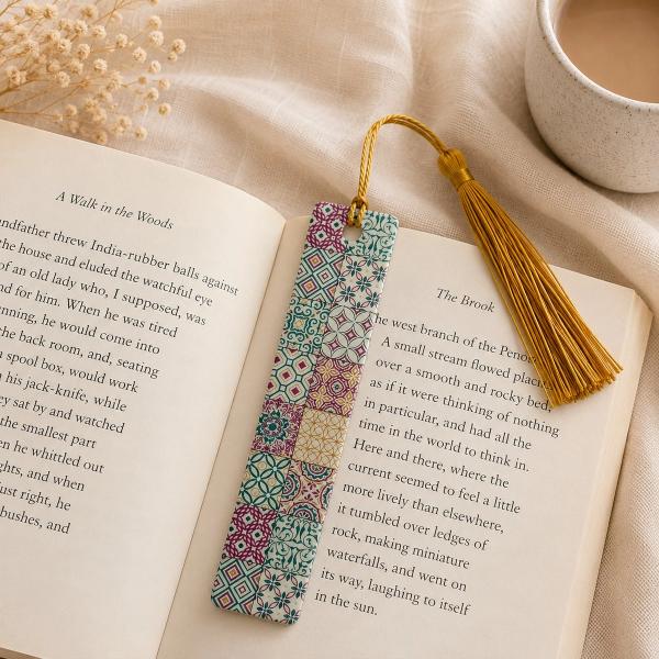 A rectangular bookmark with a colorful Moroccan mosaic tile pattern in teal, magenta, and gold, with a gold tassel, resting on an open book.