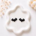 A pair of small matte black bat-shaped clay stud earrings displayed on a white ceramic tray.