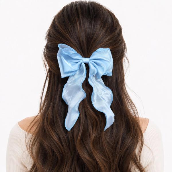 Back view of a woman wearing a large light blue satin bow clip with long flowing tails and scalloped edges in her half-up hairstyle.
