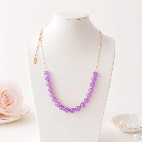 A necklace featuring a row of smooth round purple beads with gold spacers on a thin gold chain, displayed on a white jewelry bust.