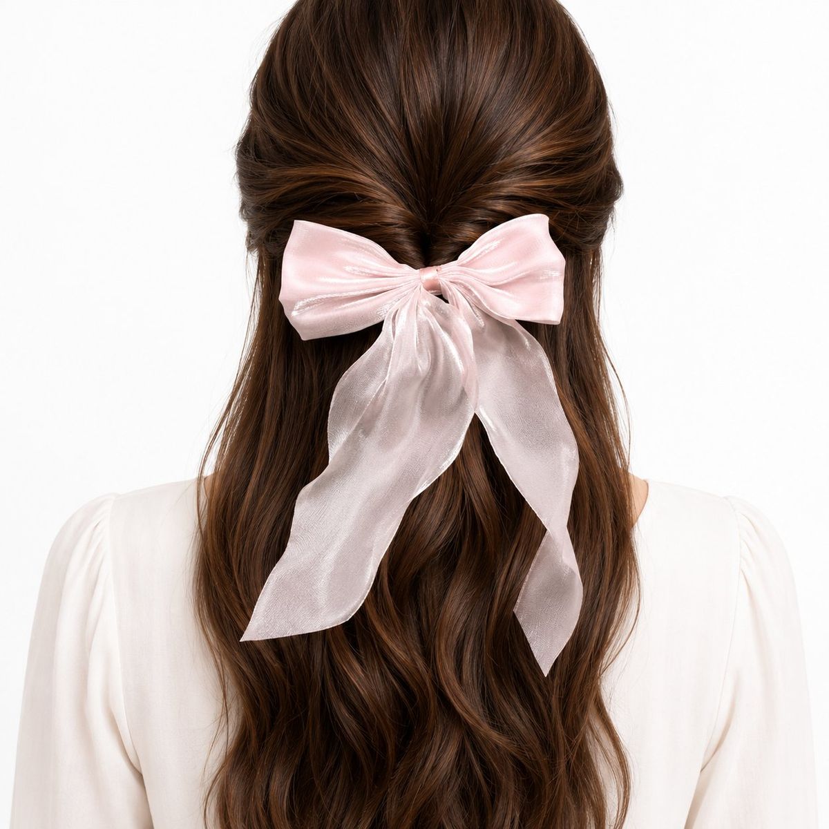 Back view of a woman with wavy brown hair wearing a large blush pink sheer organza bow clip with long flowing tails at the nape of her neck.