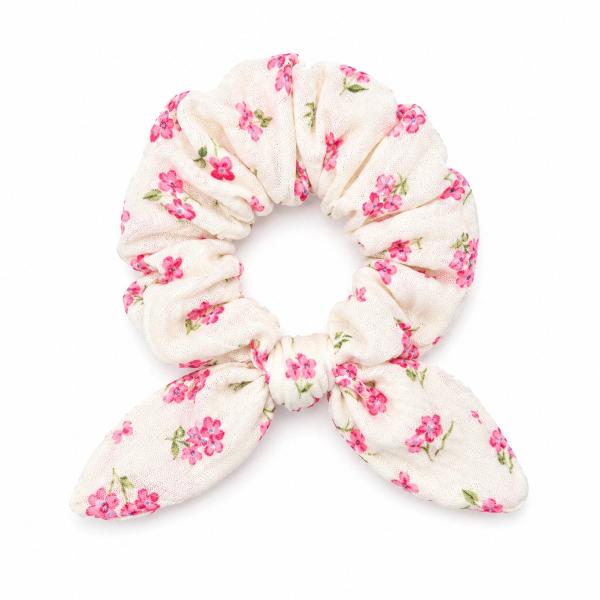 A cream fabric scrunchie with an all-over pink floral and green leaf print, featuring a gathered bow tie accent at the base.