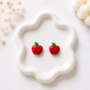 A pair of small red apple-shaped stud earrings with green leaf details displayed on a white ceramic tray.