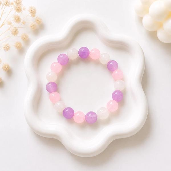 A stretch bracelet made of round beads in pink, lavender, and white arranged in an alternating pattern, displayed on a white flower-shaped ceramic tray.
