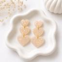Three graduating cream iridescent glitter heart-shaped clay dangles connected by gold jump rings, displayed on a white scalloped dish.