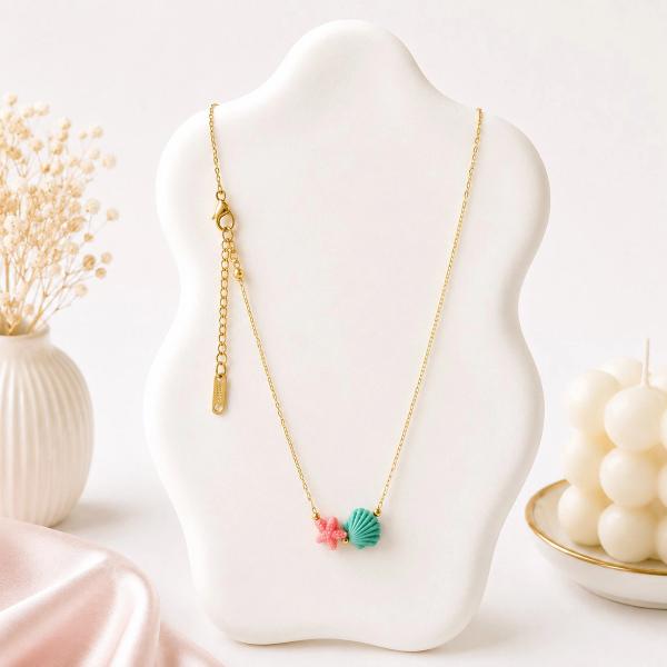 A gold chain necklace displayed on a white bust featuring a teal clay scallop shell and a pink clay starfish charm at the center.