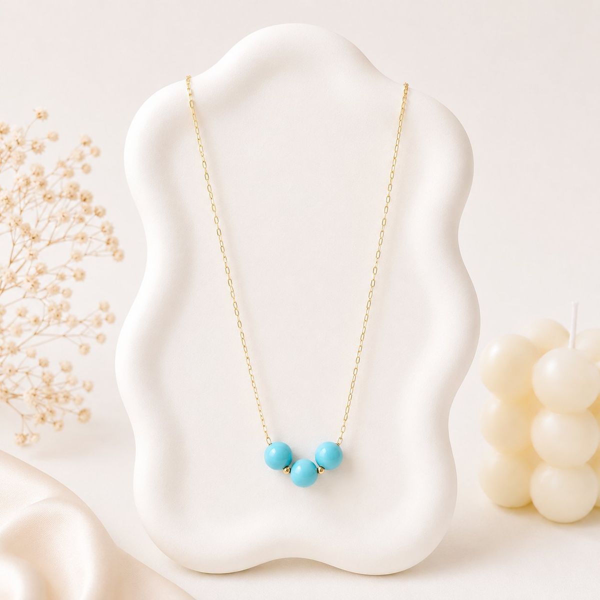 A gold-tone chain necklace with three turquoise round beads and small gold spacer beads displayed on a white wavy jewelry bust.