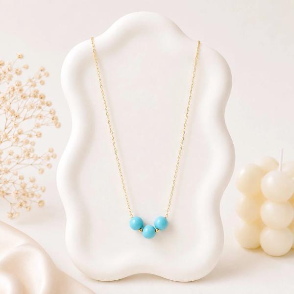 A gold-tone chain necklace with three turquoise round beads and small gold spacer beads displayed on a white wavy jewelry bust.