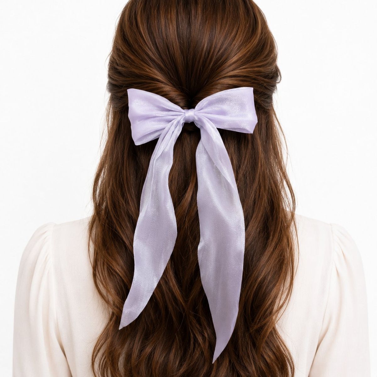Back view of a woman with brown wavy hair wearing a large sheer lavender organza bow clip with long trailing tails in a half-up hairstyle.