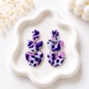 Three-tiered handmade clay dangle earrings with a white, purple, and pink terrazzo pattern connected by gold jump rings, displayed on a white ceramic tray.
