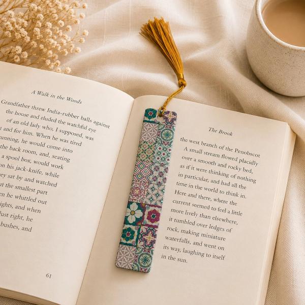 A rectangular bookmark with a colourful mosaic tile pattern in teal, pink, and purple, with a gold tassel at the top, resting on an open book.