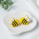 A pair of yellow and black striped bumblebee-shaped polymer clay stud earrings with white wings, displayed on a white ceramic dish.