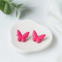 A pair of hot pink clay butterfly stud earrings resting on a white ceramic dish against a marble background.