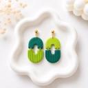 A pair of handmade clay dangle earrings with a two-part arch shape, each earring combining teal and lime green sections with vertical ribbed texture and gold-tone ball stud tops, displayed on a white ceramic tray.