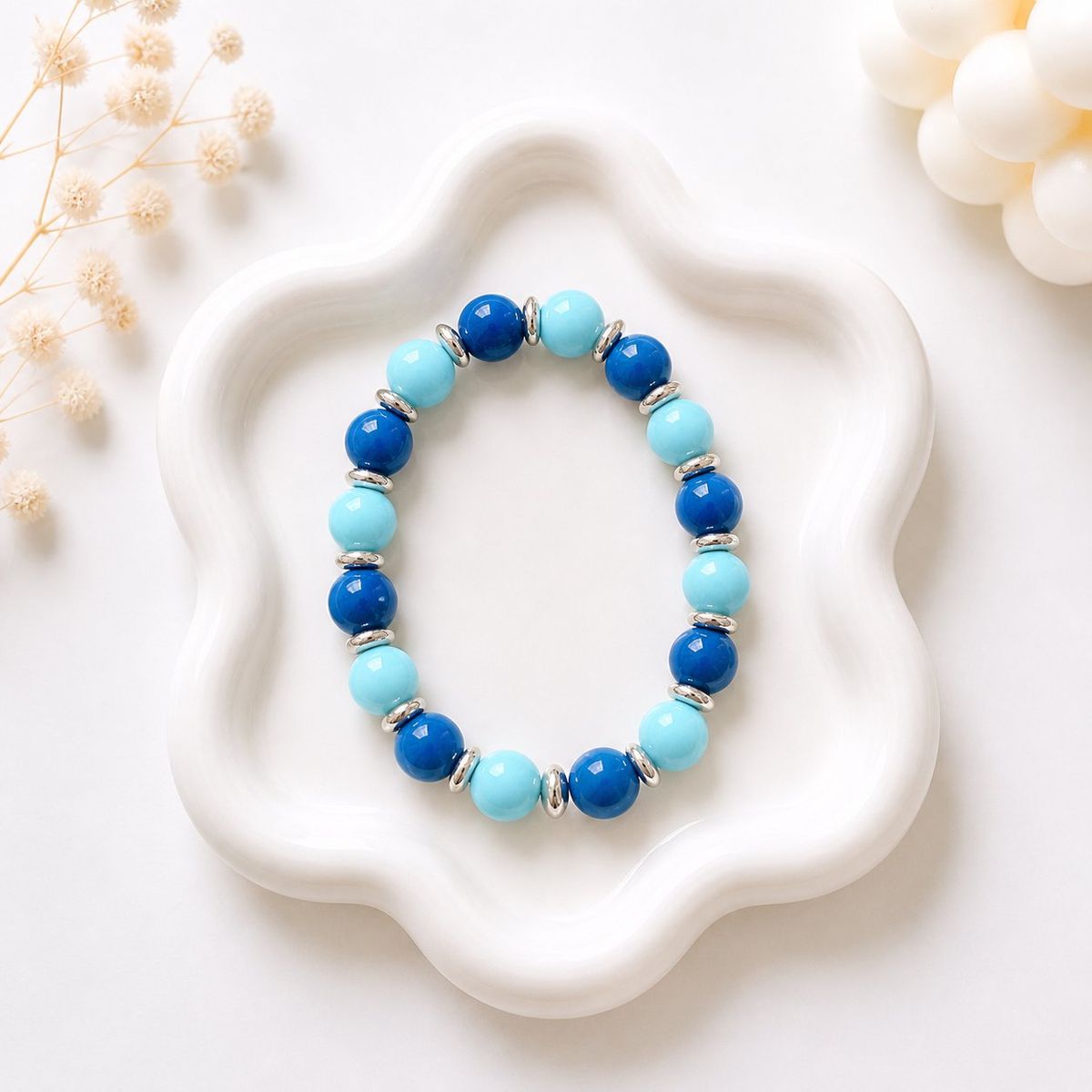 A stretch bracelet with alternating navy blue and light blue round beads separated by silver disc spacers, displayed on a white wavy ceramic tray.