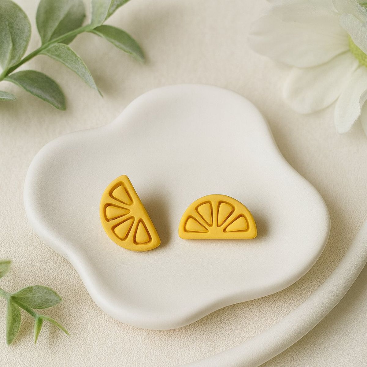 A pair of yellow polymer clay stud earrings shaped like lemon slices with etched segment lines, displayed on a white ceramic dish.