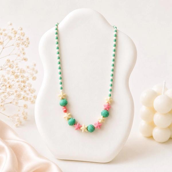 A beaded necklace displayed on a white bust featuring green clay seashell beads, pink and cream starfish charms, and alternating green and white seed beads.