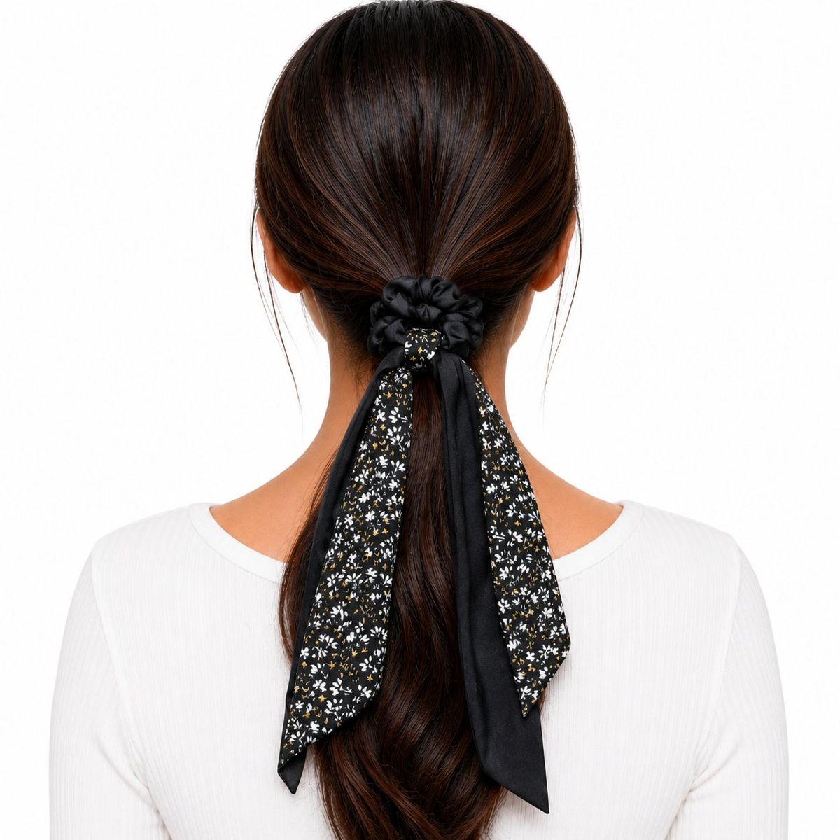 Back view of a woman with dark hair wearing a black satin scarf scrunchie with a white and gold ditsy floral print tail in a low ponytail.