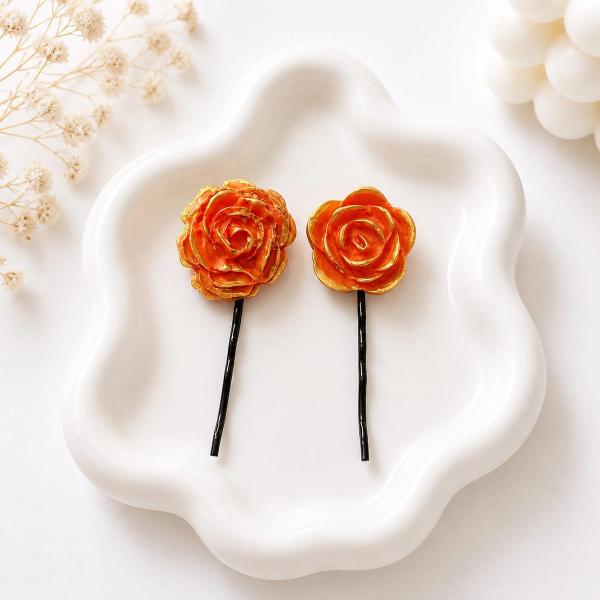 Two orange and gold clay rose bobby pins of different sizes displayed on a white ceramic tray.