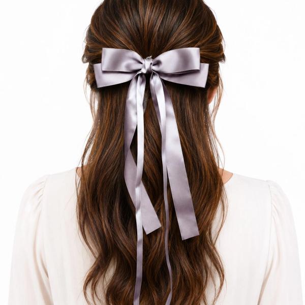 Back view of a woman wearing a large mauve-grey satin bow clip with long trailing ribbon tails in a half-up hairstyle.