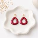 A pair of deep crimson marbled clay open teardrop dangle earrings with gold flecks, hanging from gold ball studs, displayed on a white scalloped dish.