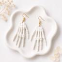 A pair of white clay skeleton hand dangle earrings with gold fishhook hardware displayed on a white ceramic tray.