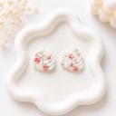 A pair of white clay knot-shaped stud earrings with a pink floral cherry blossom print, displayed on a white ceramic tray.