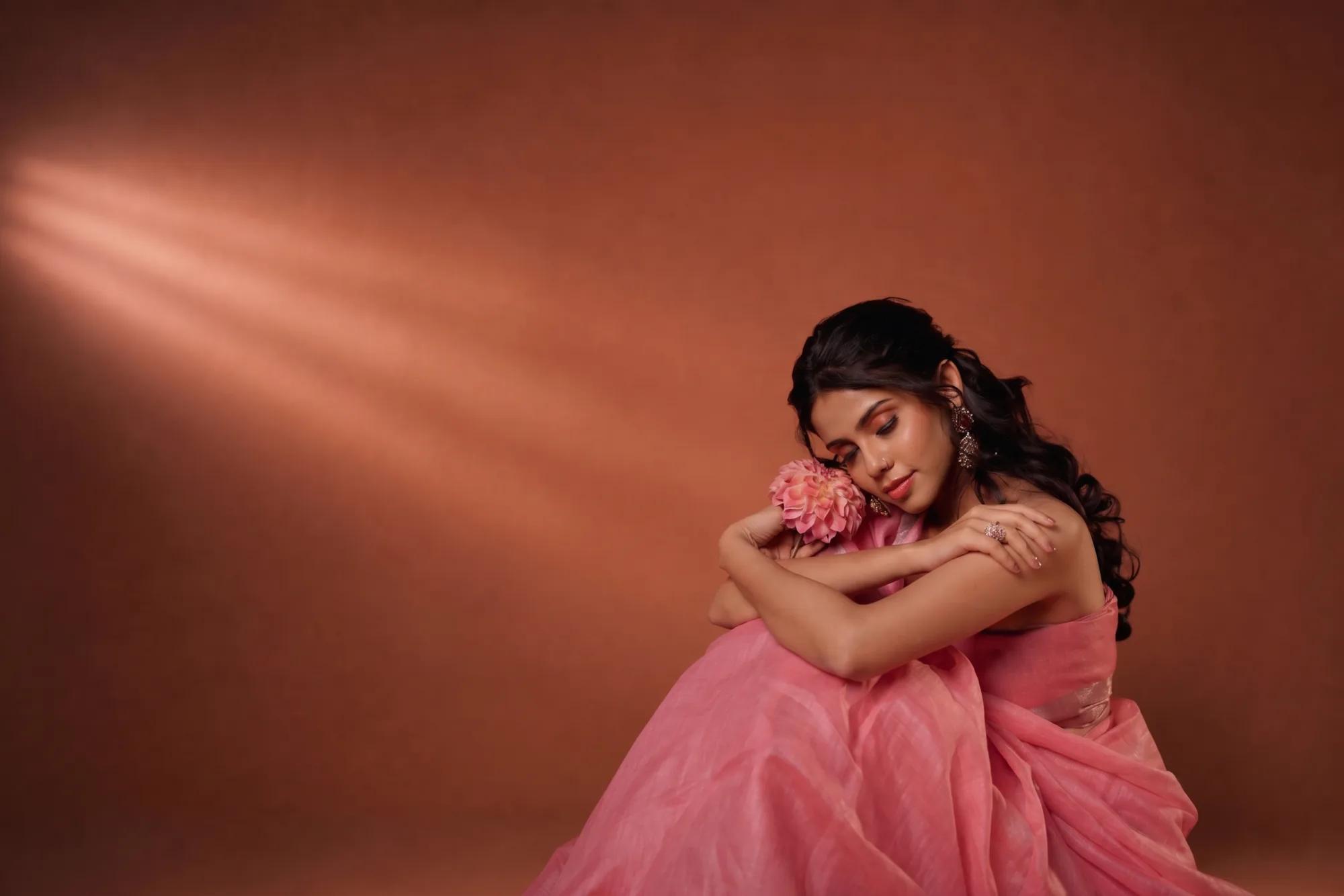 Editorial portrait with dewy skin and considered beauty, lit against a rose-clay backdrop — couture artistry by Archanaa of Kavi
