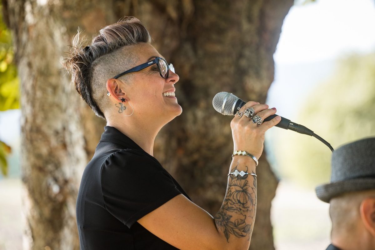Sève chante en plein air, micro à la main, avec Alex en arrière-plan.