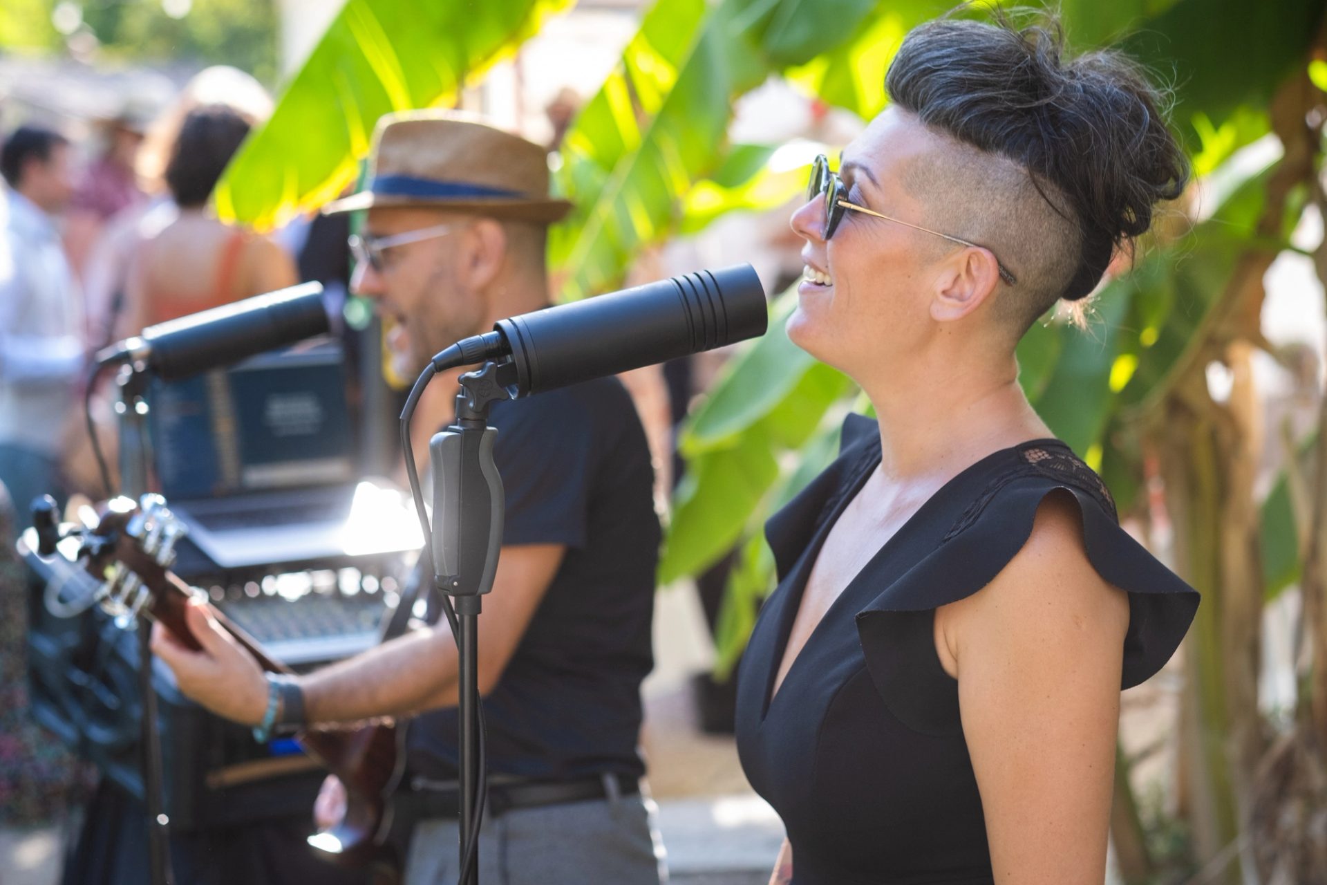 Sève chante en direct lors d’un cocktail de mariage, entourée de feuillage, invités en arrière-plan