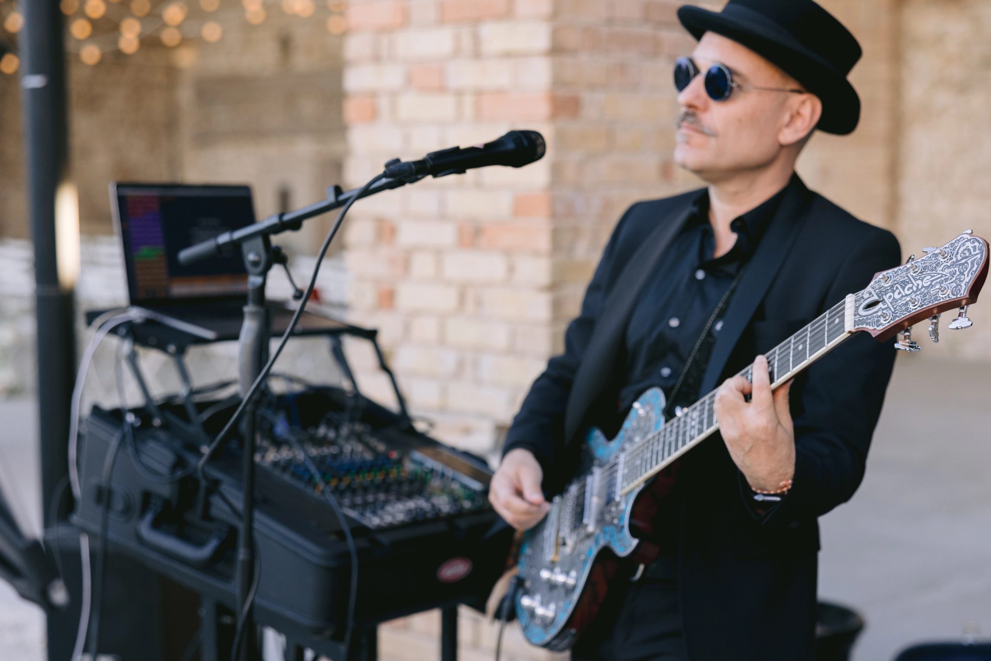Alex à la guitare électrique devant la console de son, lumières de guirlandes en fond, au Domaine de Sarson