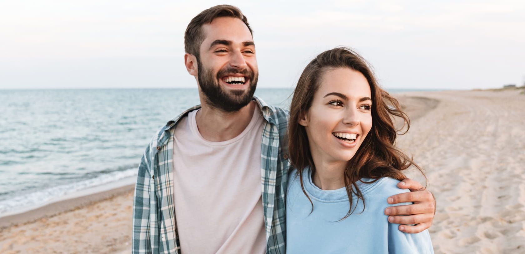 couple laughing at something in the distance at the beach