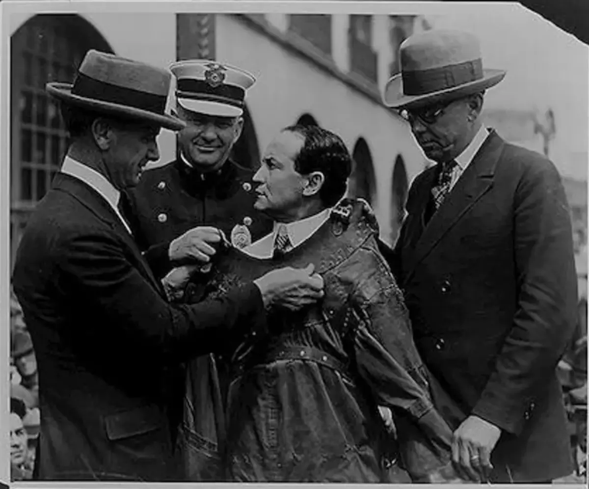 Houdini spennes fast i tvangstrøye av politibetjenter og assistenter foran et stort publikum. Library of Congress.