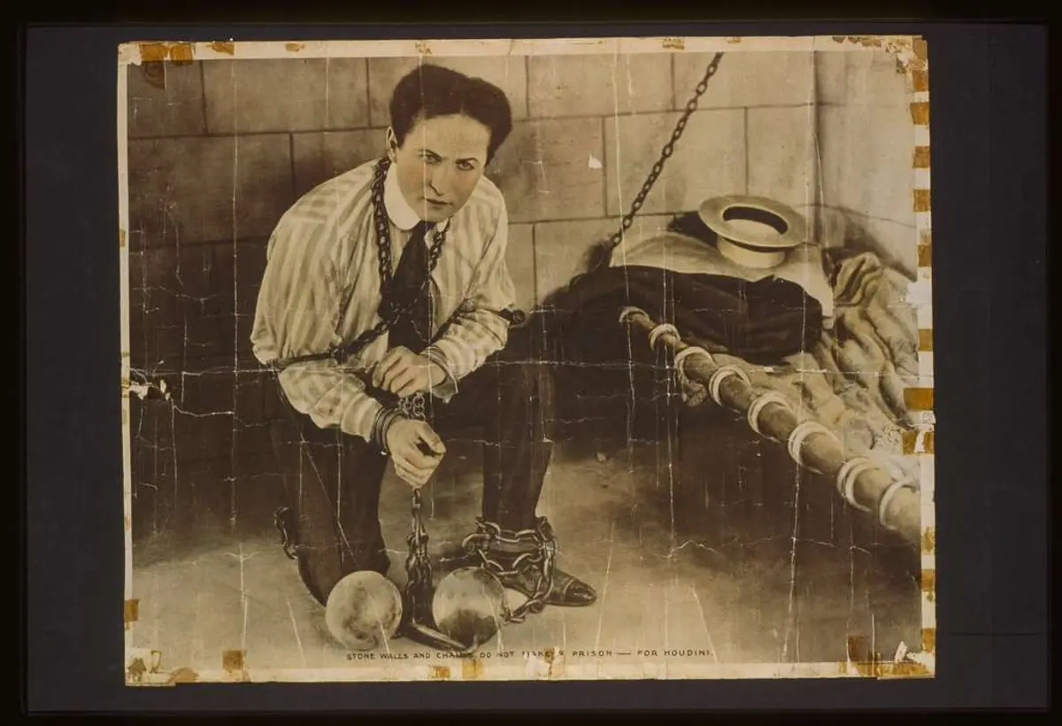 Plakat: «Stone walls and chains do not make a prison — for Houdini». Houdini sitter lenket i en celle.