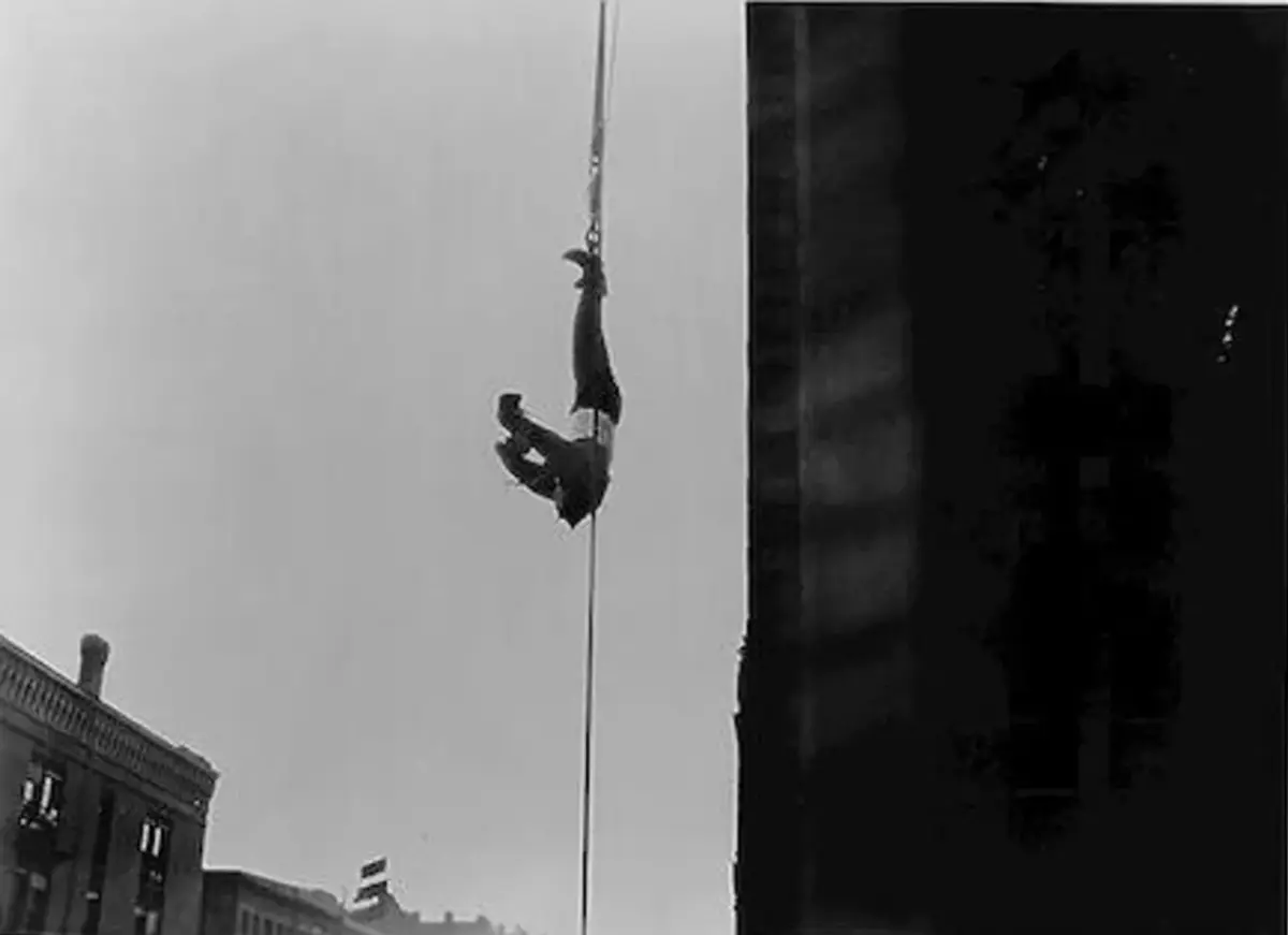 Houdini henger opp-ned fra et tau langs en amerikansk skyskraper, fastspent i tvangstrøye. Library of Congress.