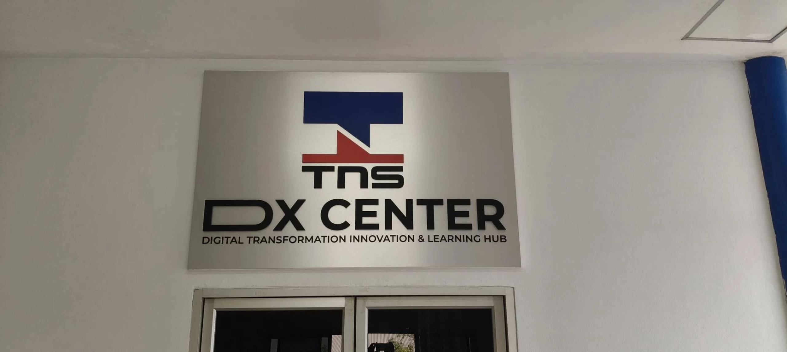 ป้ายชื่อ TNS DX Center ติดผนังภายในอาคาร | TNS DX Center name sign mounted on an interior wall