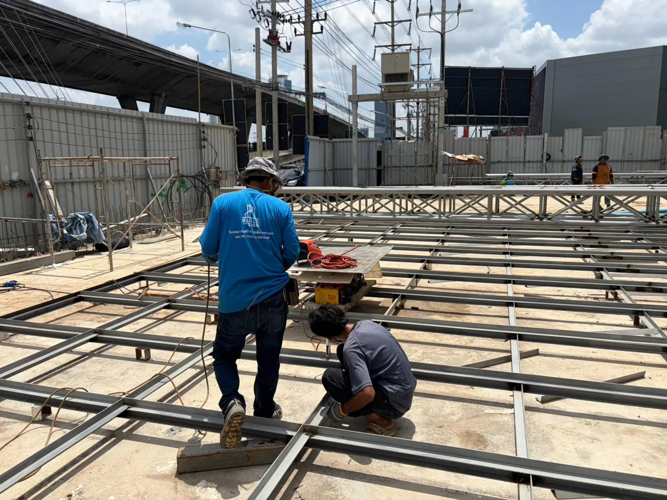 มุมกว้างงานประกอบโครงเหล็กและโครงทรัสของป้ายบิลบอร์ดบนดาดฟ้า | Wide view of billboard steel frame and truss assembly on a rooftop site - Buildandsign