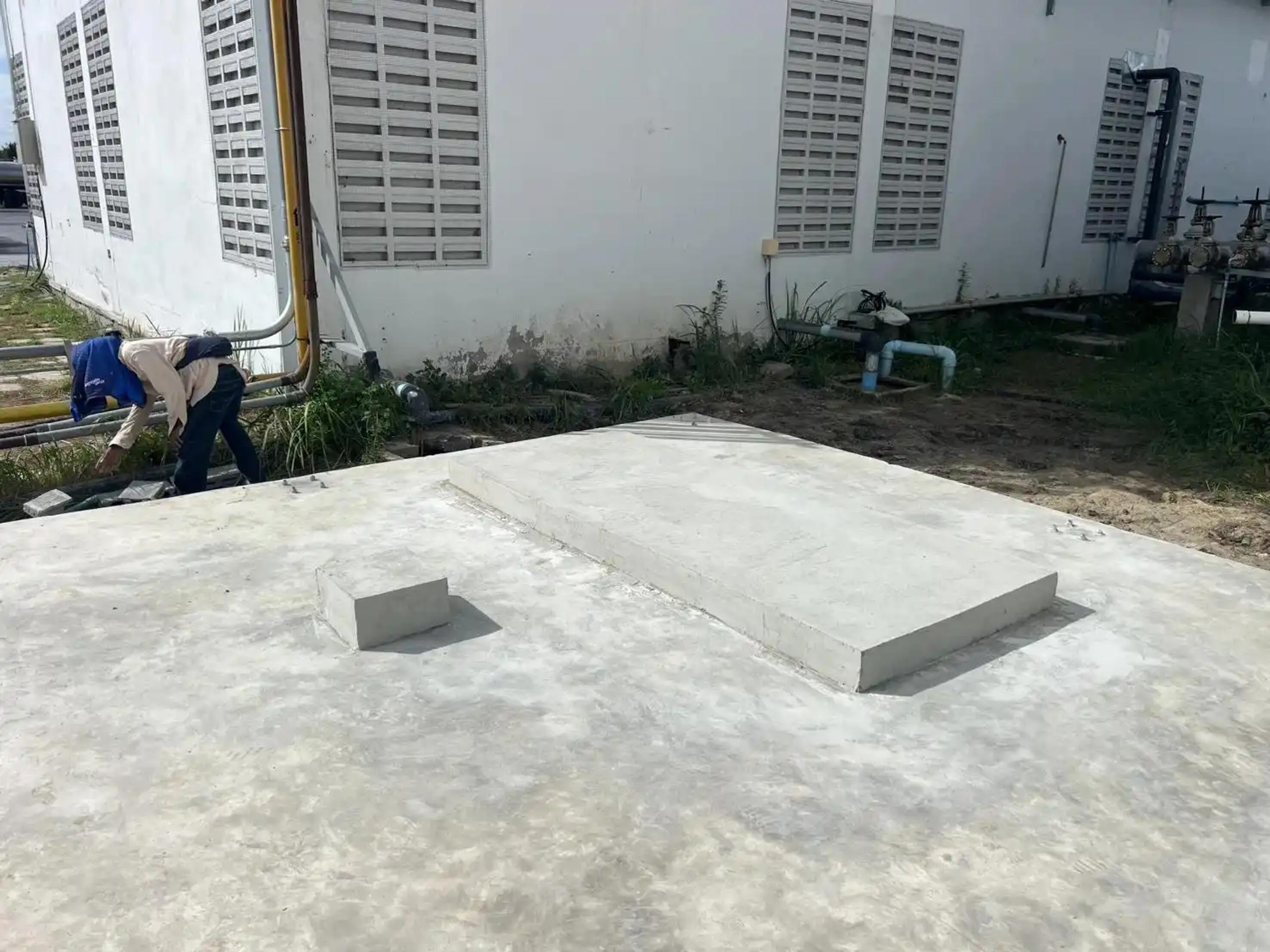 แผ่นพื้นคอนกรีตที่เทเสร็จข้างอาคารโรงงานพร้อมระบบท่อ | Finished concrete slab beside a factory building with piping systems
