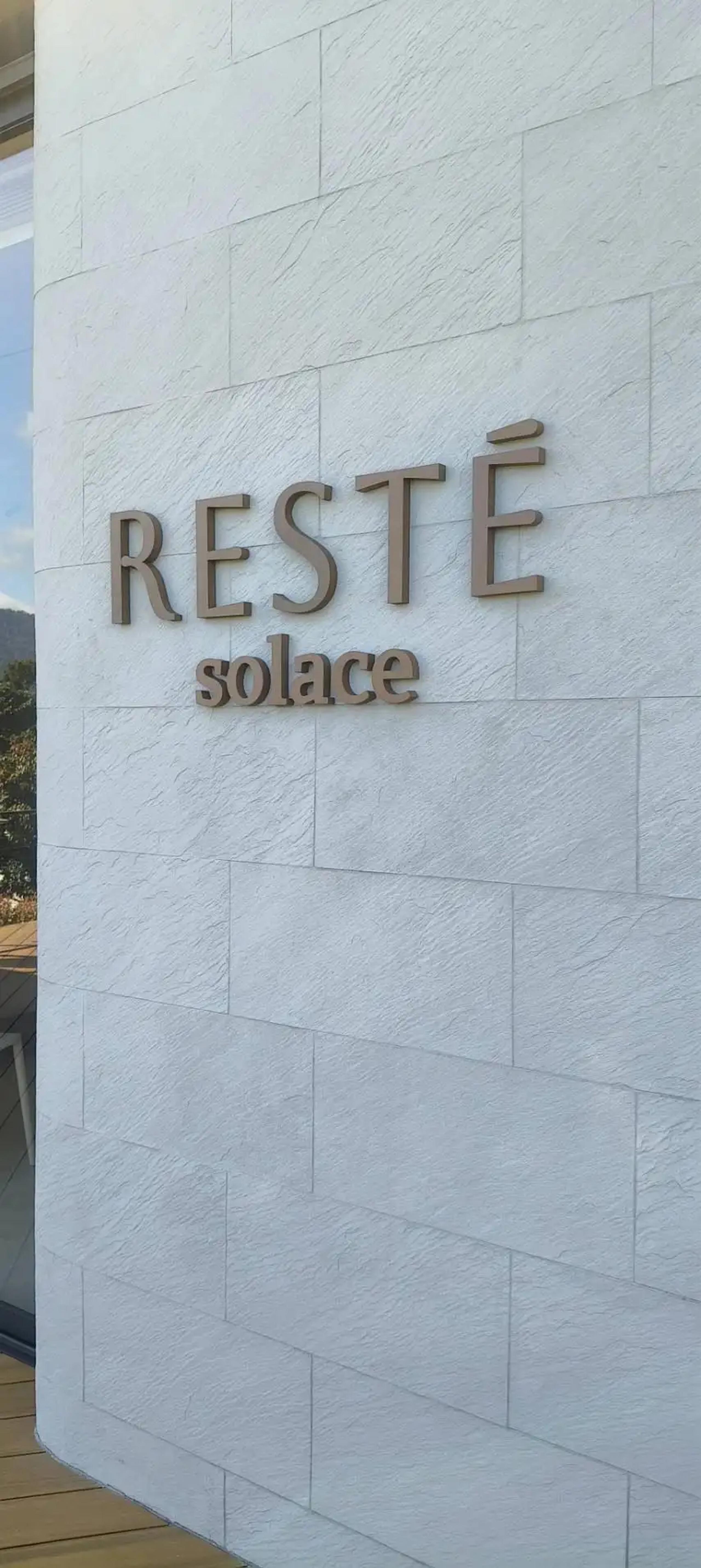 ป้ายตัวอักษรไม่มีไฟ RESTÉ solace ติดผนังหินภายนอกอาคาร | Unlit dimensional letter sign reading RESTÉ solace on an exterior stone wall