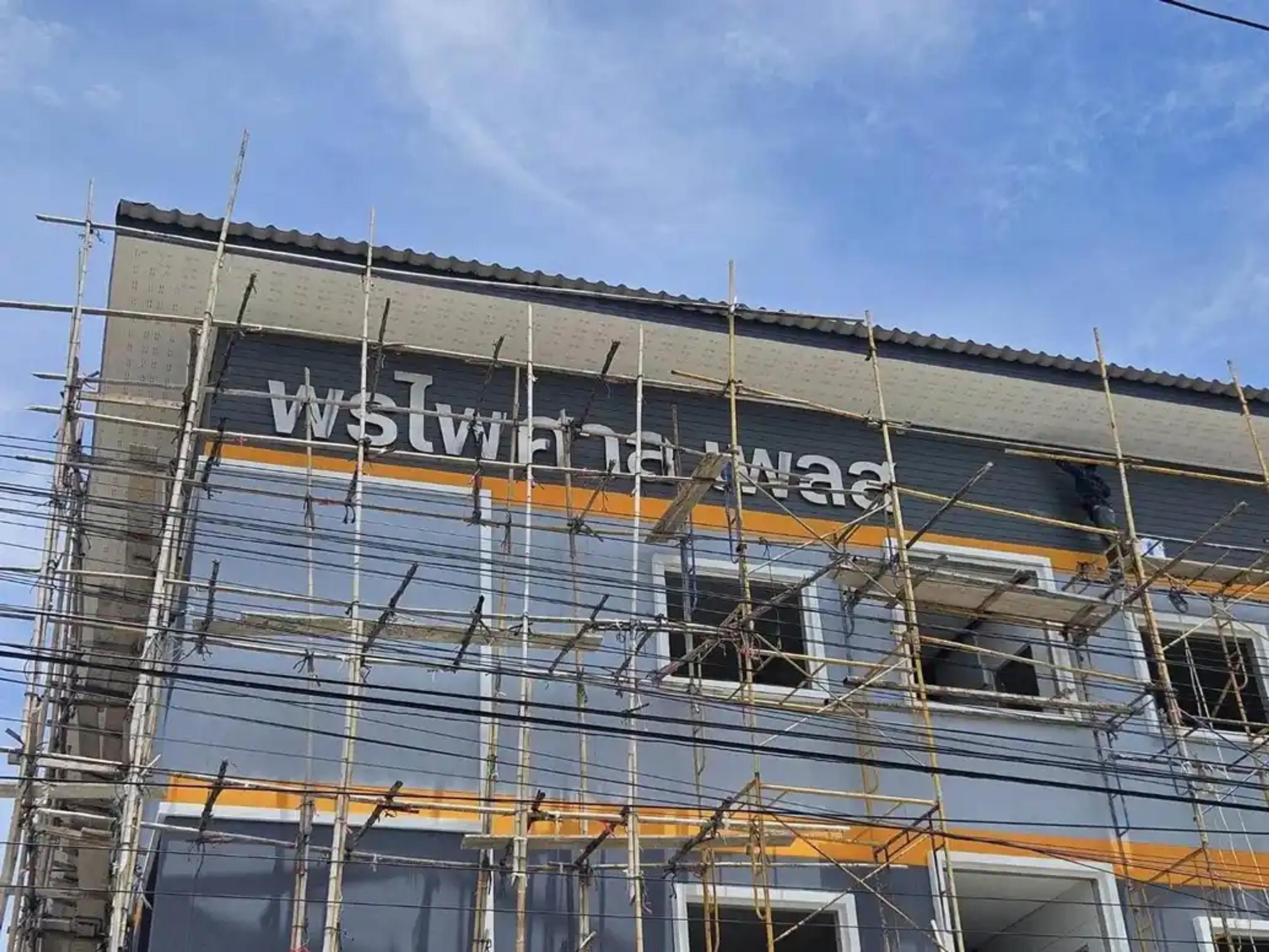 ป้ายชื่ออาคารติดตั้งบนผนังภายนอกระหว่างช่วงติดตั้งนั่งร้าน | Building name sign installed on an exterior wall during scaffolding setup