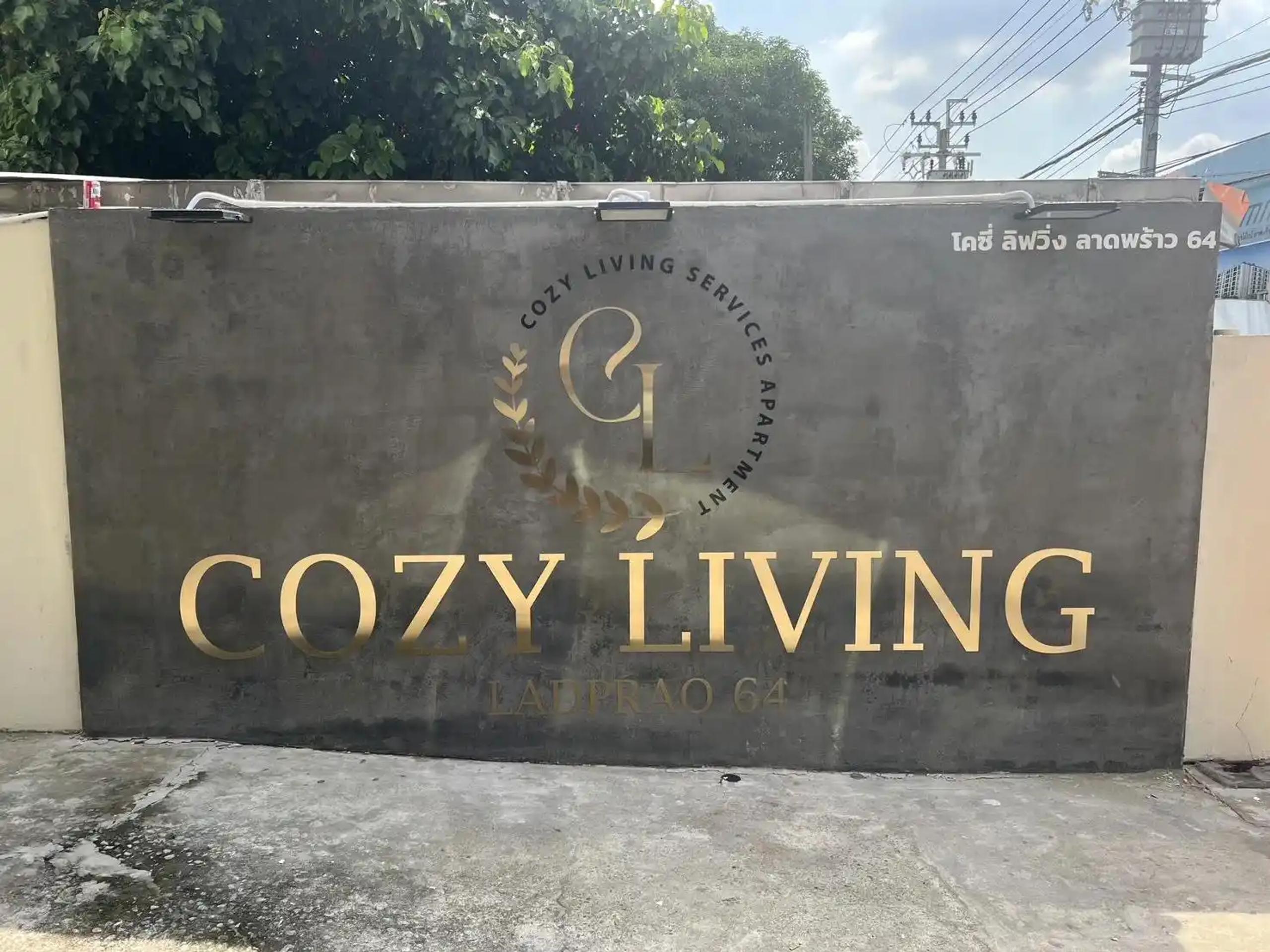 ป้ายชื่ออาคาร COZY LIVING ลาดพร้าว 64 ตัวอักษรสีทองติดผนังคอนกรีต | Gold lettering building name sign for COZY LIVING Ladprao 64 on a concrete wall