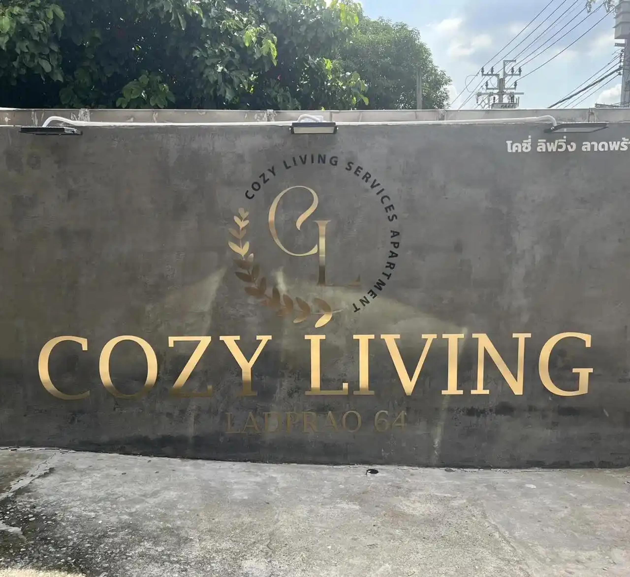 ป้ายชื่ออาคาร COZY LIVING ลาดพร้าว 64 ตัวอักษรสีทองติดผนังคอนกรีต | Gold lettering building name sign for COZY LIVING Ladprao 64 on a concrete wall