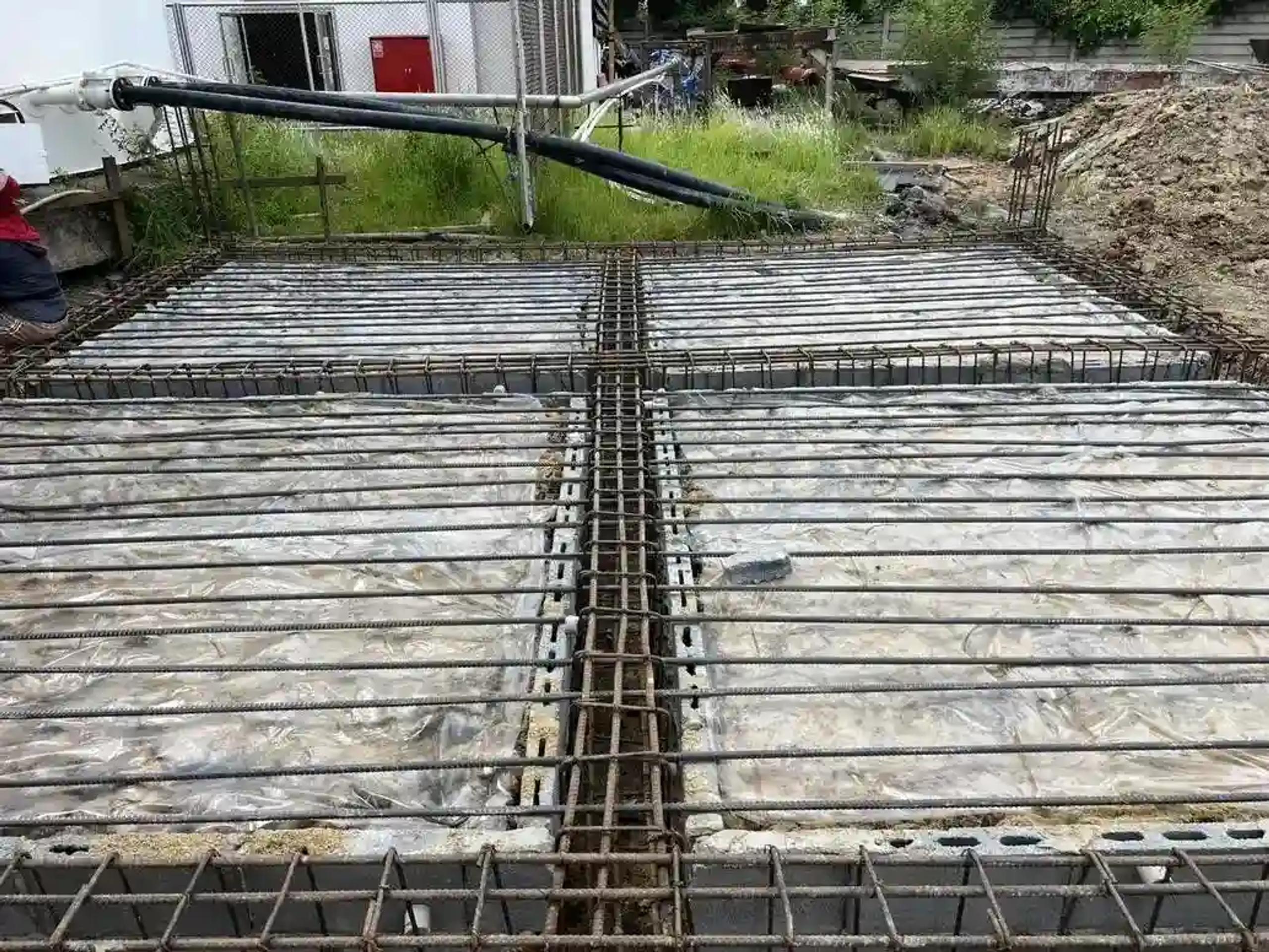 งานวางเหล็กเสริมตะแกรงสำหรับพื้นฐานรากพร้อมท่อส่งคอนกรีต | Rebar mesh laid for a foundation slab with a concrete pump hose