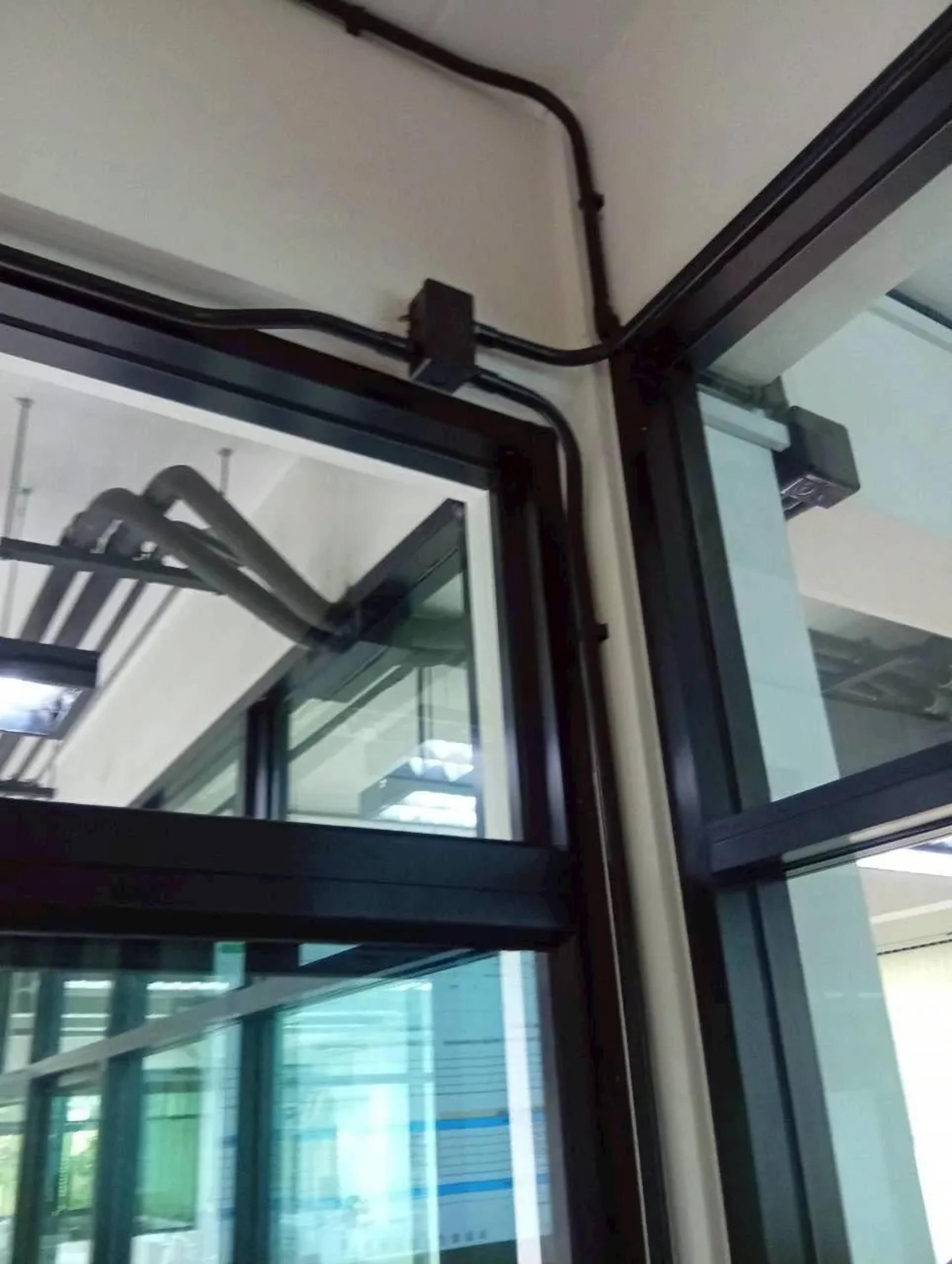 งานเดินท่อร้อยสายไฟฟ้าบริเวณมุมเพดานและกรอบประตูกระจกภายในอาคาร | Electrical conduit routed along a ceiling corner and glass door frame inside a building