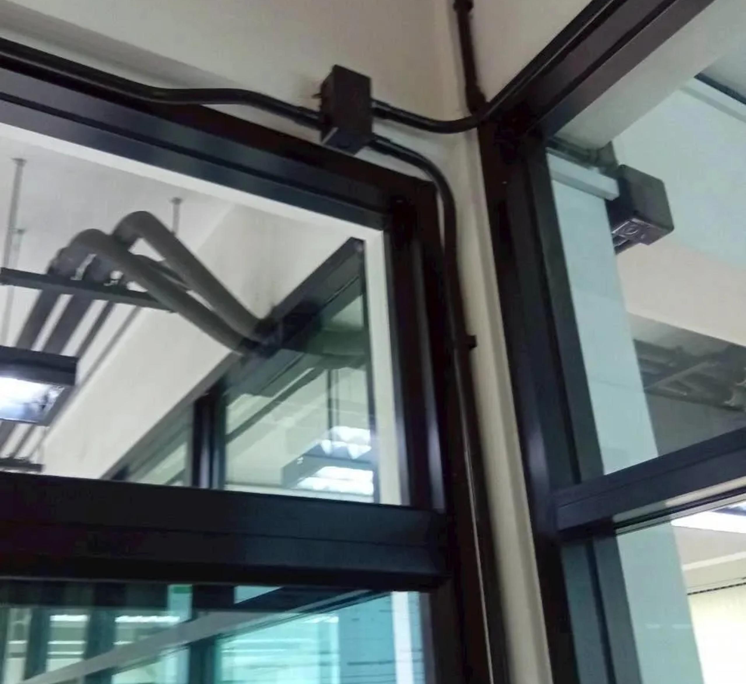 งานเดินท่อร้อยสายไฟฟ้าบริเวณมุมเพดานและกรอบประตูกระจกภายในอาคาร | Electrical conduit routed along a ceiling corner and glass door frame inside a building
